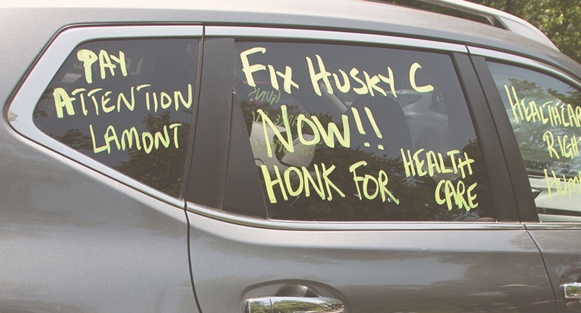 Car with writing on it that says: "Pay Attention Lamont. Fix Husky C Now!! Honk for Health Care."